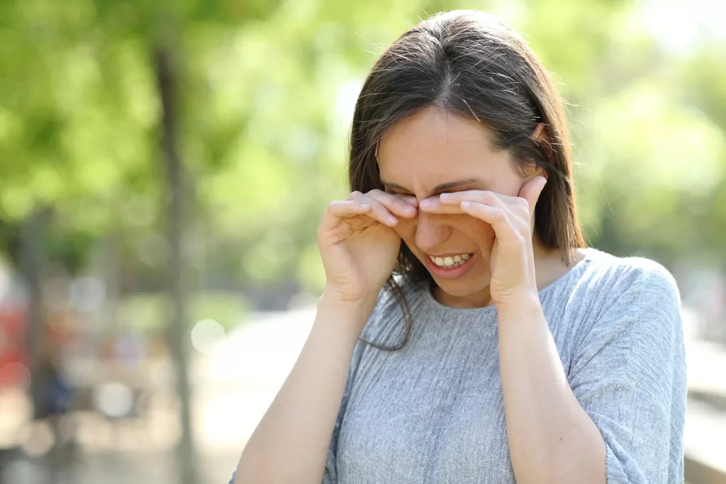 Woman with allergy rubbing her eyes while standing outdoors in a park
