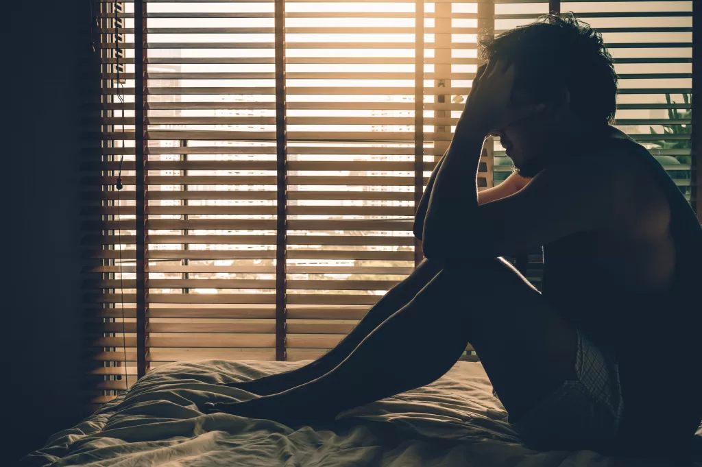 Depressed man sitting head in hands on the bed in a dark bedroom with low light environment