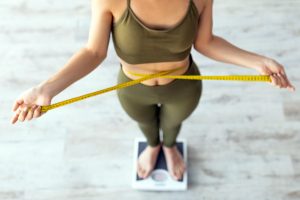 Above,View,Of,Shocked,Indian,Lady,Standing,On,Scales,,Checking Sick girl wrapped in scarf holding tissue at face and consulting doctor online on video call